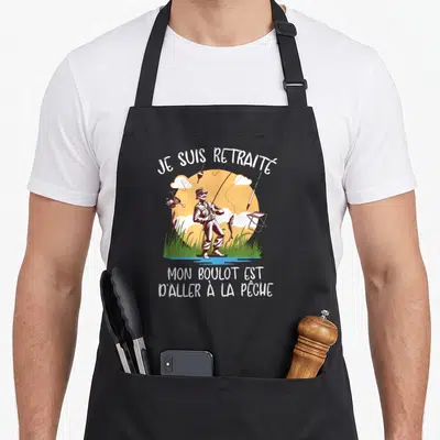 Tablier de cuisine noir avec une illustration d'un pêcheur debout dans l'eau et du texte humoristique en blanc.