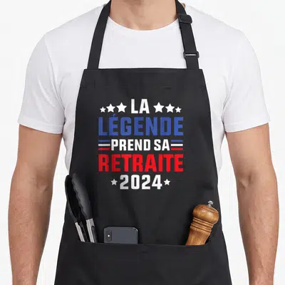 Tablier de cuisine noir avec inscription La Légende Prend Sa Retraite 2024 en bleu et rouge entouré d'étoiles blanches.