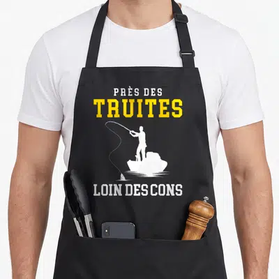 Tablier de cuisine noir avec silhouette de pecheur et le texte près des truites loin des cons en blanc et jaune.