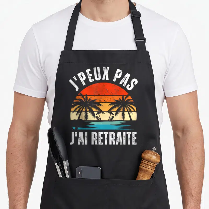 Tablier de cuisine noir avec illustration de plage et texte J'peux pas j'ai retraite en blanc.