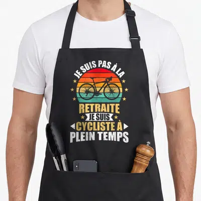 Tablier de cuisine noir avec inscription Je suis cycliste à plein temps et illustration de vélo vintage sur fond de soleil arc-en-ciel.