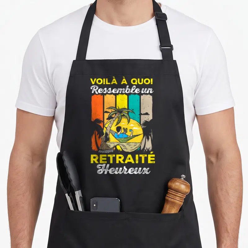 Tablier de cuisine noir avec illustration d'un homme en hamac et le texte Voilà à quoi ressemble un retraité heureux.