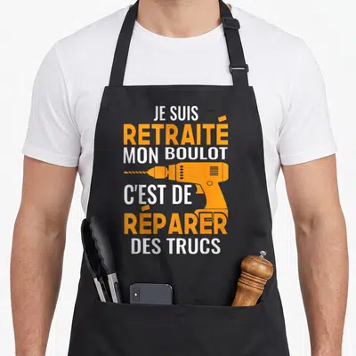Tablier de cuisine noir avec texte blanc et orange Je suis retraité mon boulot c'est de réparer des trucs et une illustration de perceuse.