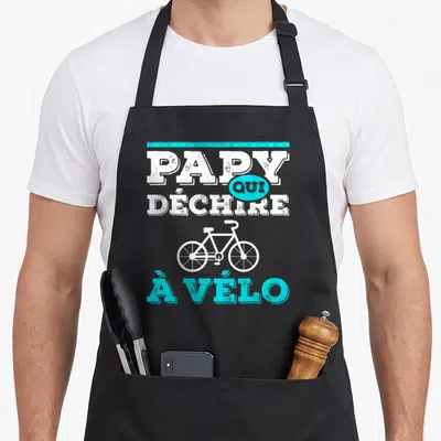 Tablier de cuisine noir avec le texte Papy qui déchire à vélo et un dessin de vélo blanc et turquoise.