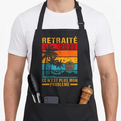 Tablier de cuisine noir avec motif rétro palmiers hamac et texte Ce n'est plus mon problème imprimé en orange.