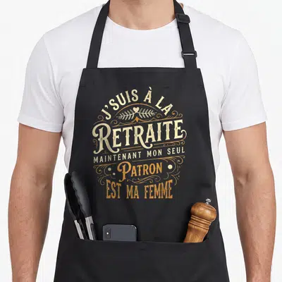 Tablier de cuisine noir avec inscription vintage J'suis à la retraite maintenant mon seul patron est ma femme orné de motifs floraux orange.