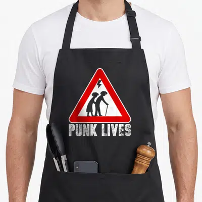 Tablier de cuisine noir avec triangle rouge signalant des silhouettes punk âgées et le texte Punk Lives en bas.