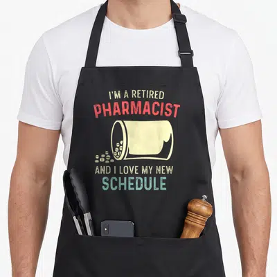 Tablier de cuisine noir avec illustration de flacon de médicaments et texte humoristique sur la retraite professionnelle.
