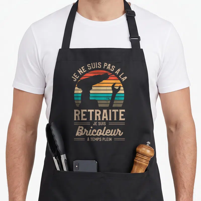 Tablier de cuisine noir avec inscription vintage et silhouette d'étau et clé anglaise sur fond de soleil rayé.