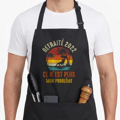 Tablier de cuisine noir avec illustration de plage et texte Ce n'est plus mon problème imprimé en orange et jaune.