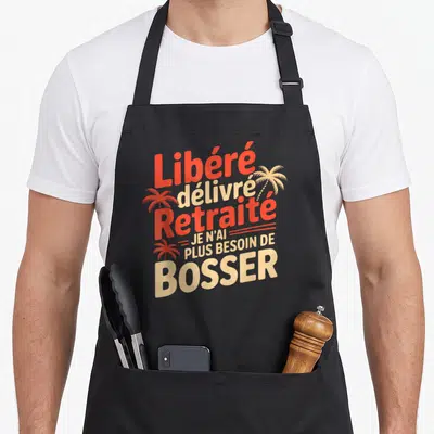 Tablier de cuisine noir avec inscription colorée libéré délivré retraité et illustrations de palmiers tropicaux.
