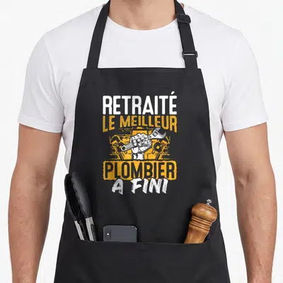 Tablier de cuisine noir avec poing tenant une clé à molette et texte blanc et orange sur fond gris uni.