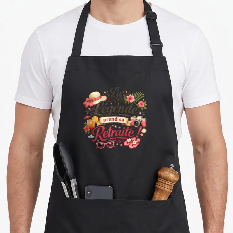 Tablier de cuisine noir avec inscription La Légende prend sa Retraite entourée d'un cocktail, d'un chapeau et de fleurs tropicales.