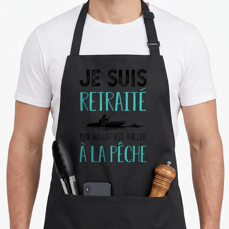 Tablier de cuisine noir avec l'inscription Je suis retraité mon boulot est d'aller à la pêche et une silhouette de bateau.