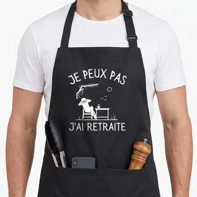 Tablier de cuisine noir avec une silhouette relaxant et le texte Je peux pas j'ai retraite imprimé en blanc.