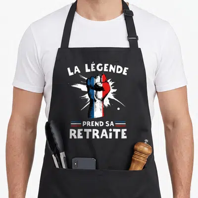 Tablier de cuisine noir avec un poing tricolore et le texte La Légende Prend Sa Retraite 2023 imprimé en blanc.