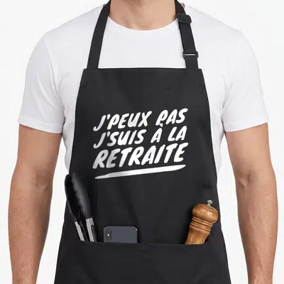 Tablier de cuisine noir avec l'inscription blanche J'peux pas j'suis à la retraite en typographie manuscrite.