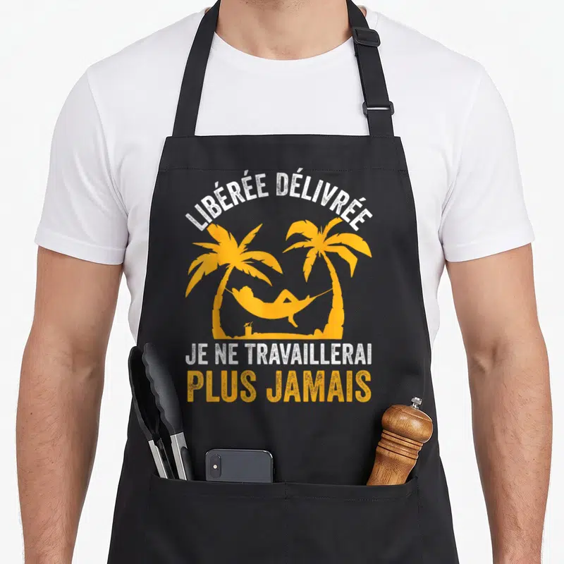 Tablier de cuisine noir avec une silhouette orange dans un hamac sous des palmiers et le texte Libérée Délivrée Je Ne Travaillerai Plus Jamais en blanc et orange.