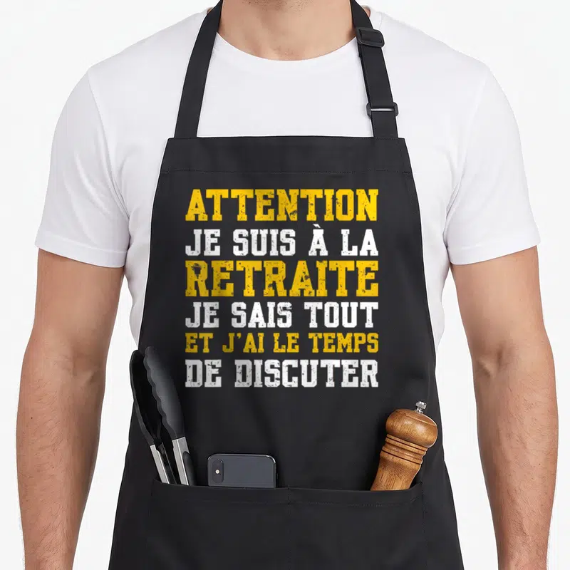 Tablier de cuisine noir avec texte Attention Je Suis À La Retraite Je Sais Tout En jaune et blanc sur fond uni.