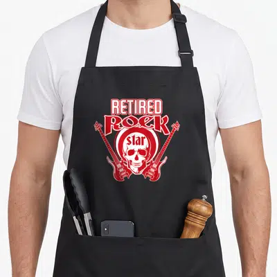 Tablier de cuisine noir avec un crâne blanc entouré de guitares rouges et le texte Retired Rock Star.