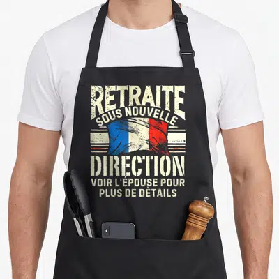 Tablier de cuisine noir avec inscription retraite sous nouvelle direction et drapeau français stylisé au centre du motif imprimé.