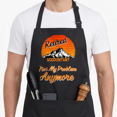 Tablier de cuisine noir avec motif soleil orange, montagne et texte Retired Accountant Not My Problem Anymore en lettres stylisées.