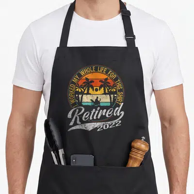 Tablier de cuisine noir avec illustration rétro de plage et texte Retired 2022 en blanc.