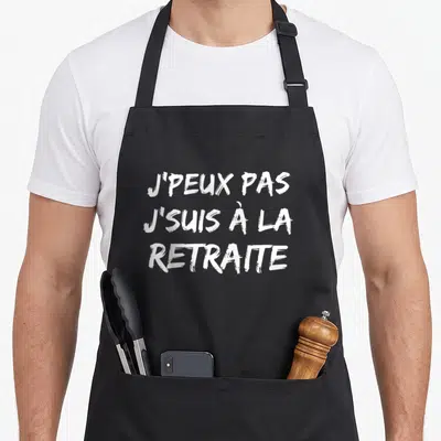 Tablier de cuisine noir avec inscription blanche J'peux pas j'suis à la Retraite en typographie manuscrite.