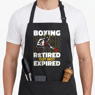 Tablier de cuisine noir avec illustration d'un boxeur et texte Boxing Legend Retired But Not Expired en blanc et jaune.