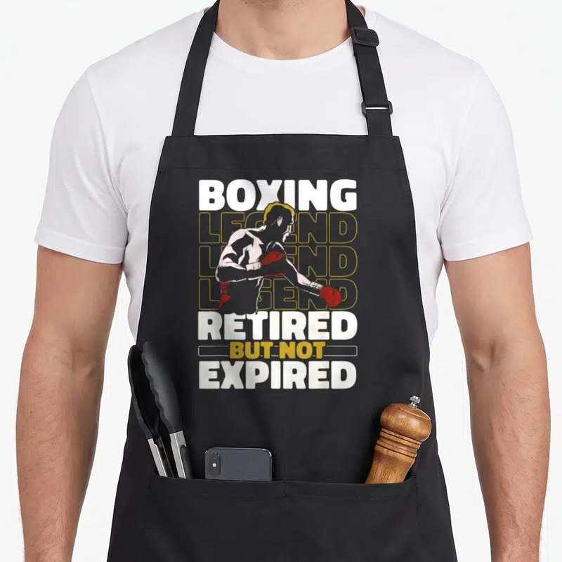 Tablier de cuisine noir avec illustration d'un boxeur et texte Boxing Legend Retired But Not Expired en blanc et jaune.