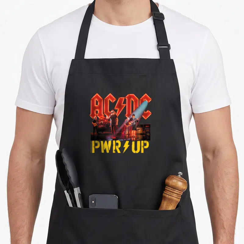 Tablier de cuisine noir avec logo AC/DC rouge, photo de concert et texte PWRUP jaune