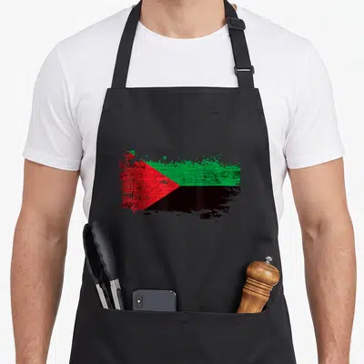 Tablier de cuisine noir avec un drapeau Martinque stylisé en rouge vert et noir effet éclaboussure.