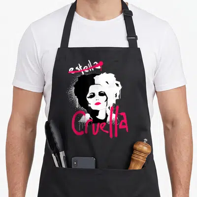 Tablier de cuisine noir avec illustration Cruella Estella au visage bichromique et lettrage spray pink vif.