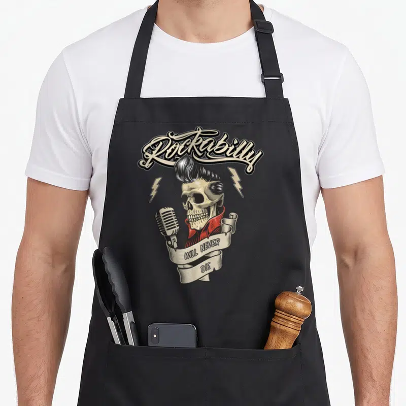 Tablier de cuisine noir avec illustration crâne Rockabilly coiffé en pompadour tenant un micro vintage sous une banderole.