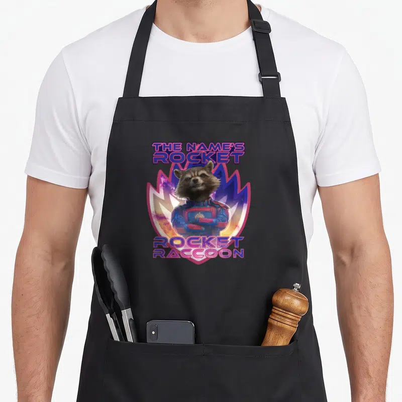 Tablier de cuisine noir avec le renard spatial Rocket Raccoon et le texte The Name's Rocket en lettres colorées.