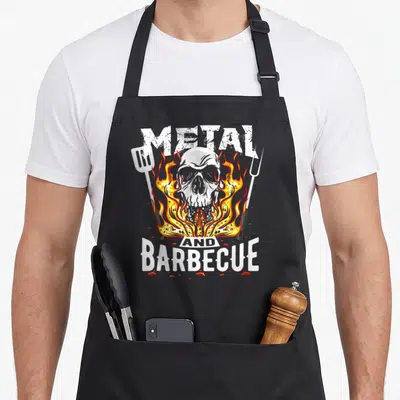 Tablier de cuisine noir avec un crâne enflammé, une spatule, une fourche et les mots Metal and Barbecue en blanc.