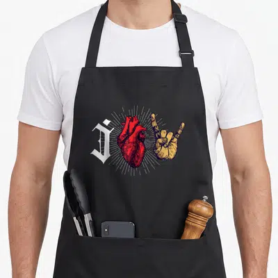 Tablier de cuisine noir avec cœur anatomique rouge, main en signe de metal jaune et lettre gothique blanche.