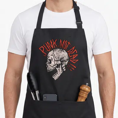 Tablier de cuisine noir avec un crâne gris et l'inscription Punk Not Dead en rouge au style graffiti.