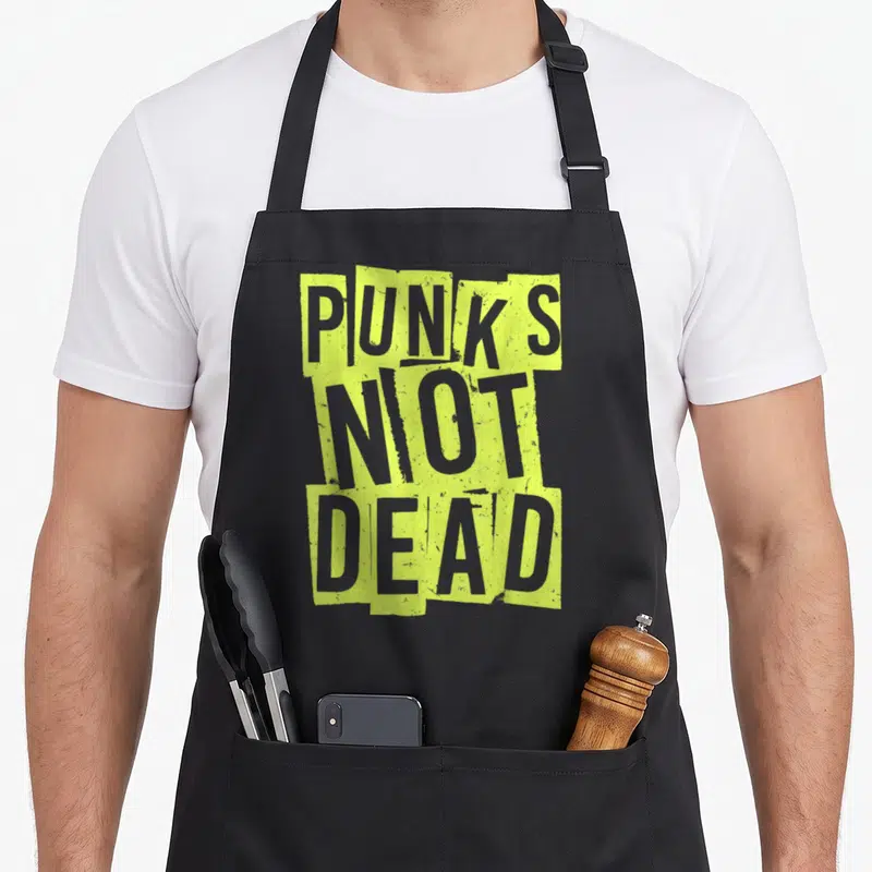 Tablier de cuisine noir avec inscription Punk's Not Dead en jaune fluo et gris texturé.