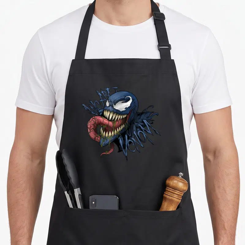 Tablier de cuisine noir avec illustration de Venom montrant sa langue et les mots We are Venom en arrière-plan.