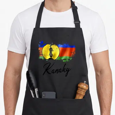 Tablier de cuisine noir avec drapeau Kanak style grunge et inscription Kanaky en écriture cursive noire.
