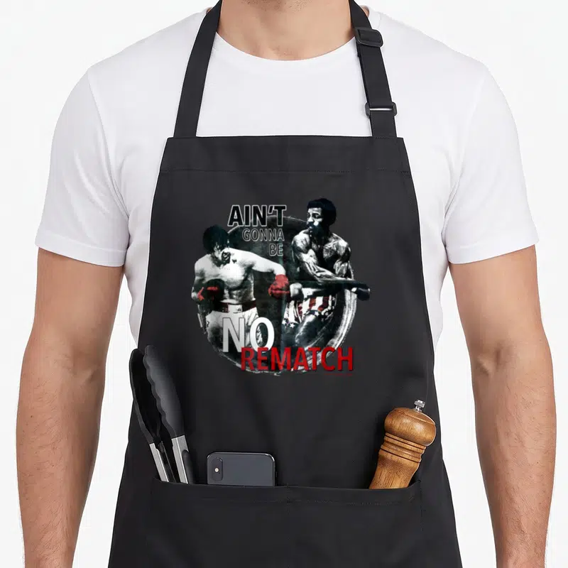 Tablier de cuisine noir avec illustration de deux boxeurs et le texte Ain't Gonna Be No Rematch en noir et rouge.