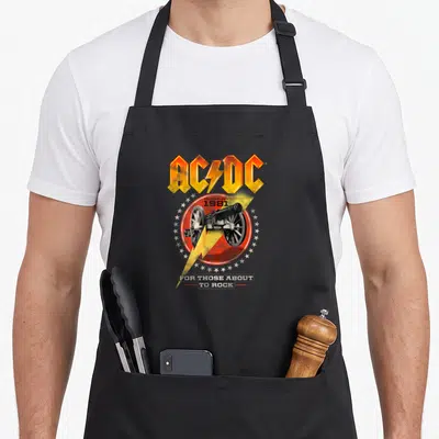 Tablier de cuisine noir avec le logo AC/DC, un canon et une foudre jaune imprimés au centre.