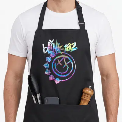 Tablier de cuisine noir avec logo Blink 182 coloré, smiley aux yeux en X et flèches directionnelles sur fond uni.