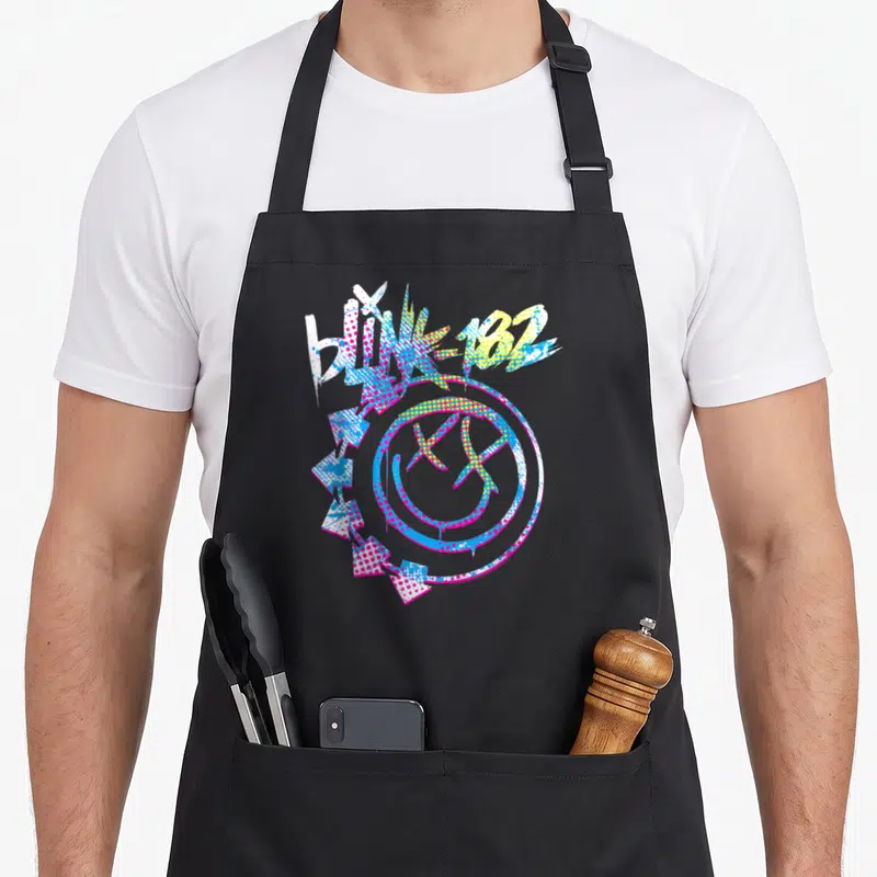 Tablier de cuisine noir avec logo Blink 182 coloré, smiley aux yeux en X et flèches directionnelles sur fond uni.