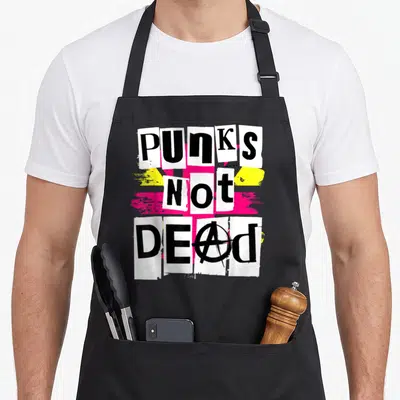 Tablier de cuisine noir avec design Punks Not Dead en lettres découpées sur fonds rose et jaune vif.