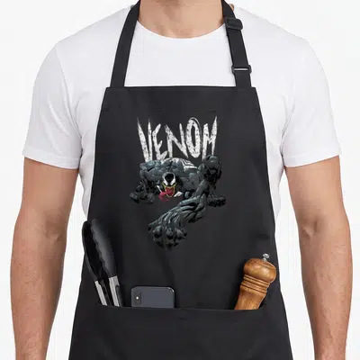 Tablier de cuisine noir avec illustration de Venom accroupi, langue sortie et logo Venom en lettres blanches stylisées au-dessus.