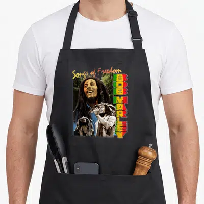 Tablier de cuisine noir avec portrait de Bob Marley, dreadlocks et texte vertical Bob Marley aux couleurs vert jaune rouge.