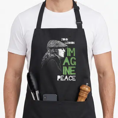 Tablier de cuisine noir avec portrait de John Lennon et texte Imagine Peace en vert et blanc.