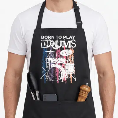 Tablier de cuisine noir avec illustration de kit de batterie et texte Born To Play Drums en style vintage coloré.
